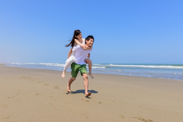 彼女をオンブして砂浜を走っている彼氏