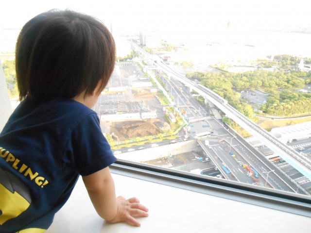 高い部屋の窓から外を眺めている子ども(飛行機からみる地上のイメージ)