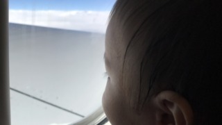 フライト中の飛行機の窓から外を見ている赤ちゃん