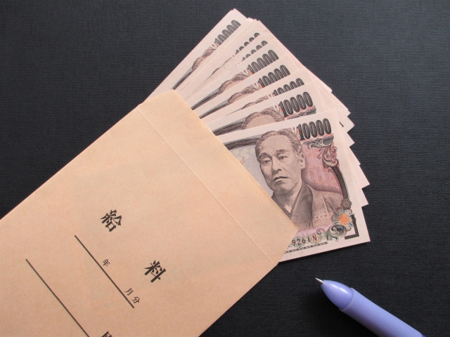 給料と書かれた茶封筒に一万円札が10枚以上入っている。その横に青いボールペンが置いてある。
